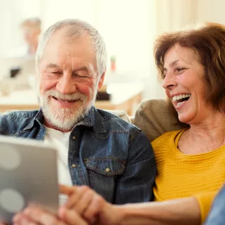 An older couple laughing together over a tablet